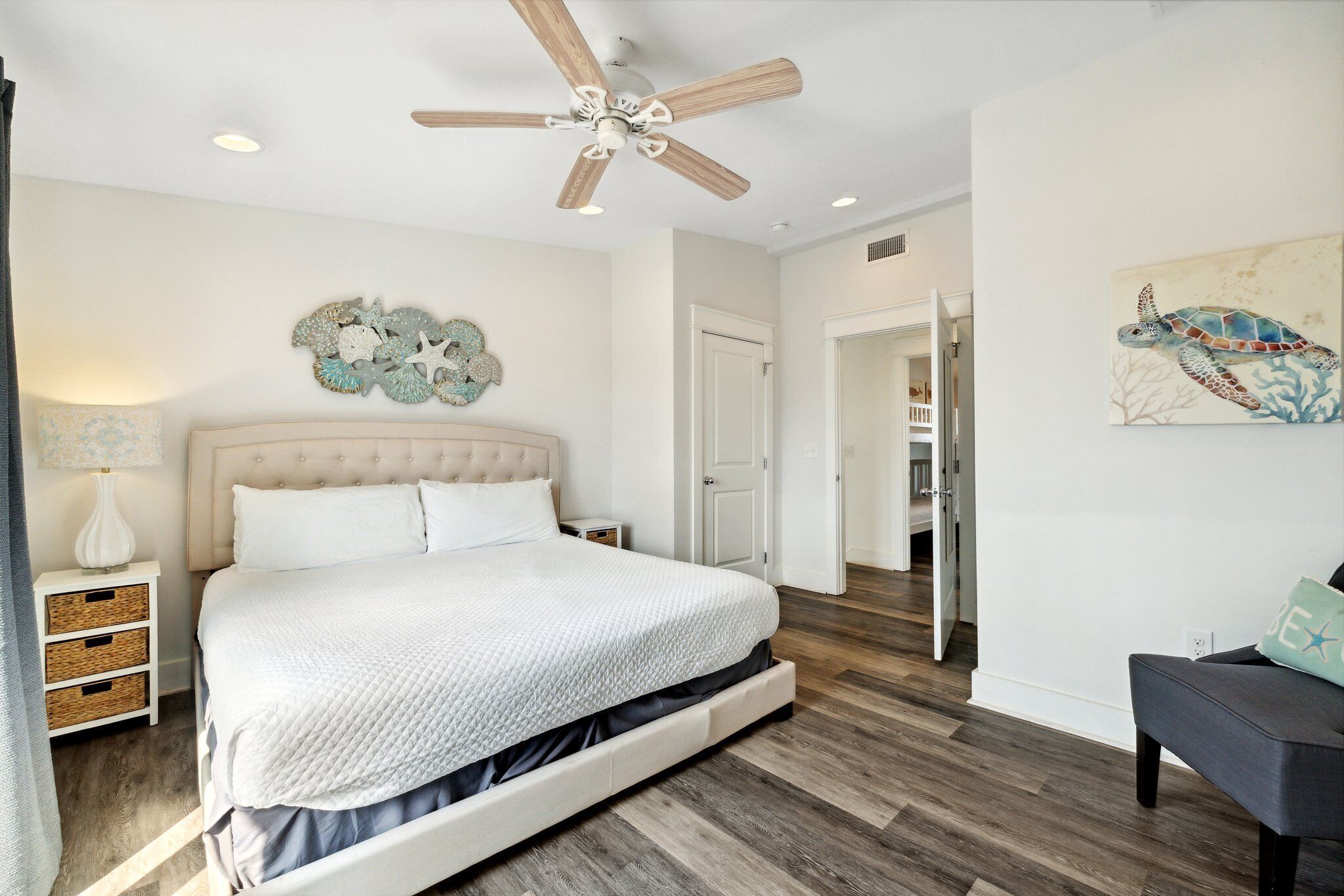 Une chambre à coucher comprenant un lit, un ventilateur de plafond, un élément de décoration murale et une porte donnant sur une autre pièce.