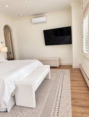 A bedroom with a bed, a bench, a TV mounted on the wall, and an air conditioning unit. - True Ski in Ski Out Located In Arrowhead village. 3 Bed / 3 Bath Unit (Edwards)