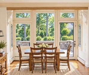 A dining area with a wooden table and chairs, large windows with a view of greenery, and a stone wall outside. - True Ski in Ski Out Located In Arrowhead village. 3 Bed / 3 Bath Unit (Edwards)