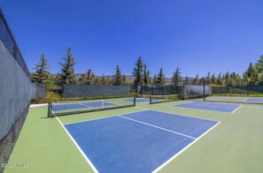 Un court de tennis extérieur doté de plusieurs terrains, entouré d’arbres et offrant une vue sur un ciel dégagé.