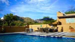 Un espace piscine avec vue sur les montagnes, des meubles d’extérieur et un mur recouvert de cactus.