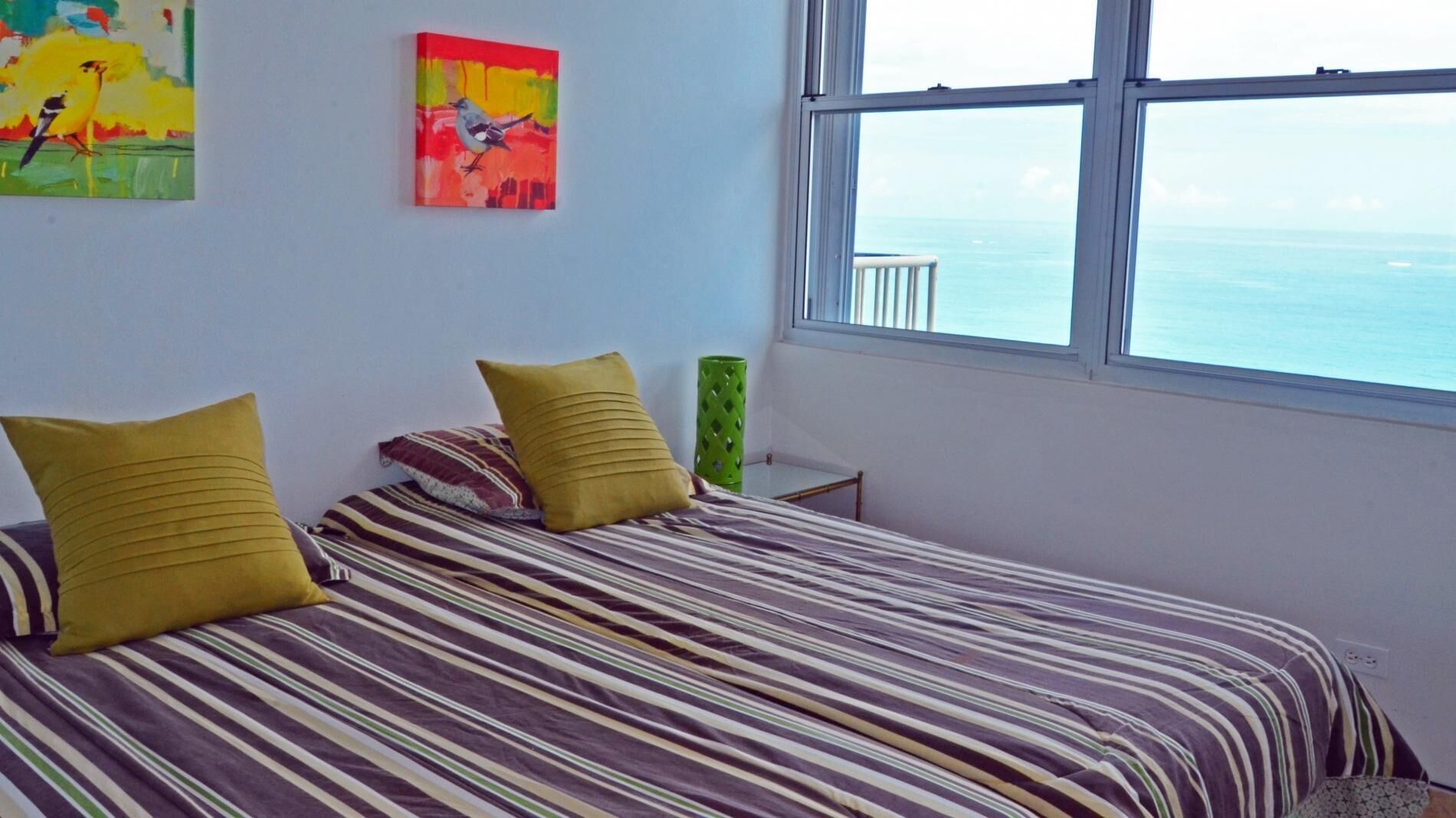 Une chambre à coucher avec un lit, deux oreillers, un vase vert et deux tableaux accrochés au mur.