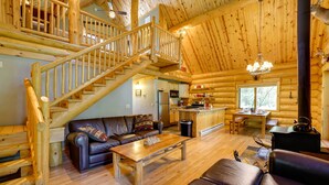A log cabin interior with a wooden staircase, leather sofas, a wooden dining table, and a kitchen area. - Secluded Log Cabin in NW Michigan: Hot Tub & Deck (Hersey)