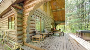 A log cabin with a wooden deck, outdoor seating, and a hot tub. - Secluded Log Cabin in NW Michigan: Hot Tub & Deck (Hersey)