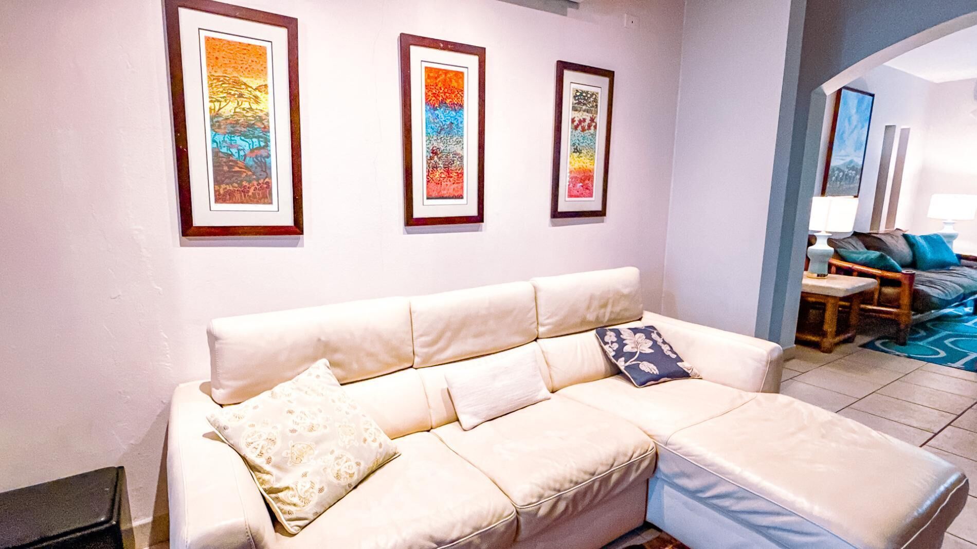Un salon avec un canapé beige, trois œuvres d’art encadrées accrochées au mur et un tapis bleu à motifs.