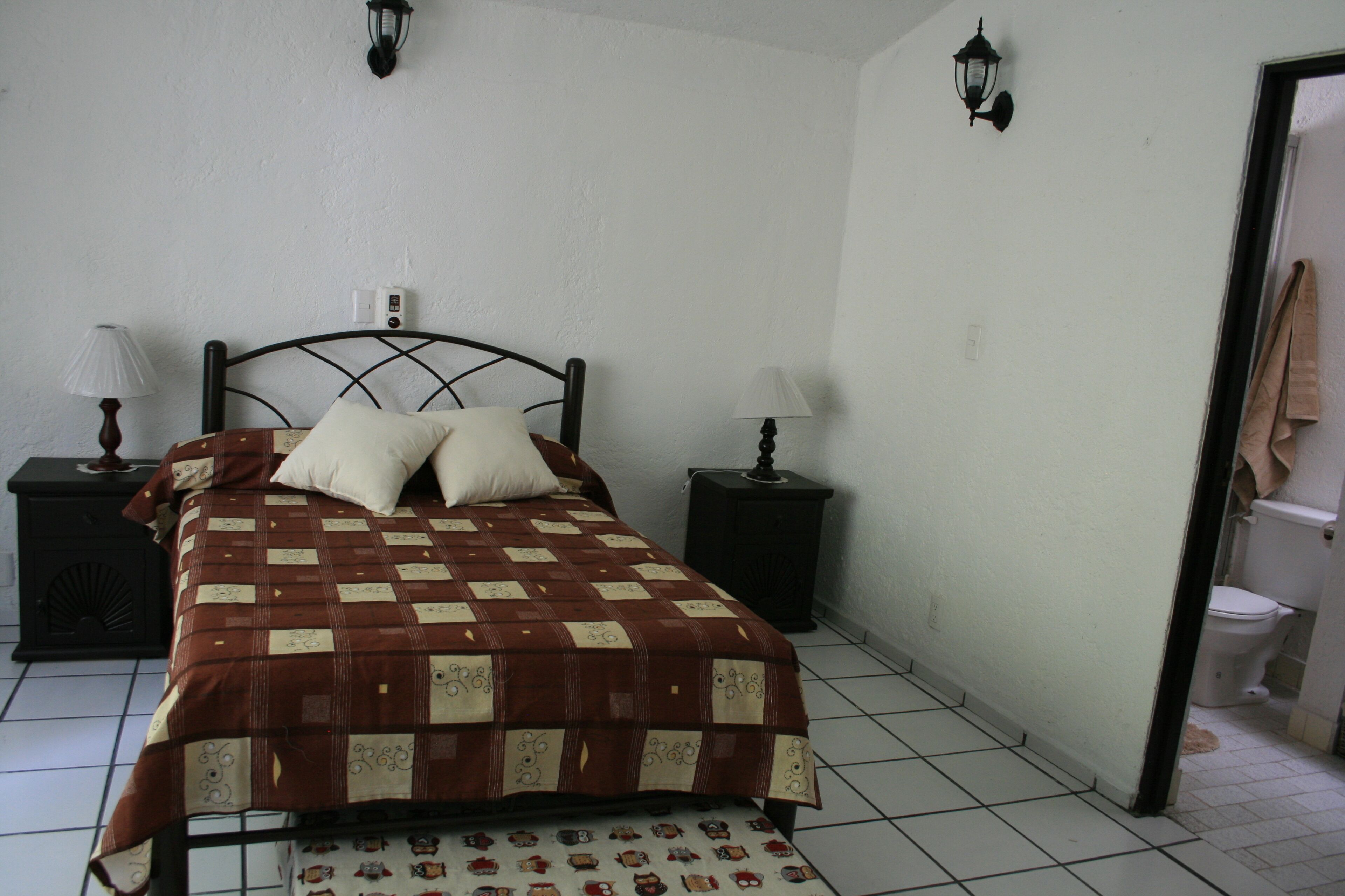 Una camera da letto con un letto, due comodini, una lampada a muro e una porta che dà su un bagno.