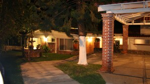 A residential house at night with a well-lit front yard, a brick pillar, and a covered porch.