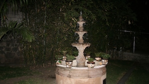 A stone fountain with multiple tiers and water spouts, surrounded by potted plants.