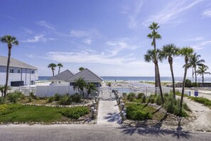 A beachfront property with a gated entrance, a pathway leading to a beach area, and palm trees.