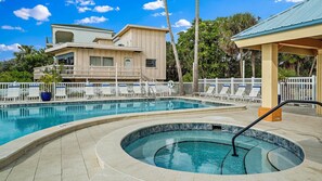 Una piscina con sillones de descanso y un jacuzzi, rodeada por una valla y palmeras.