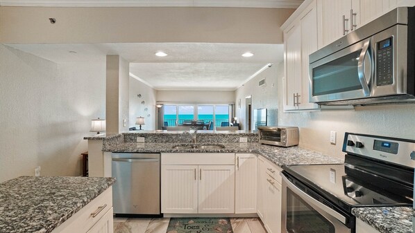 A kitchen with granite countertops, stainless steel appliances, and a view to the outside.