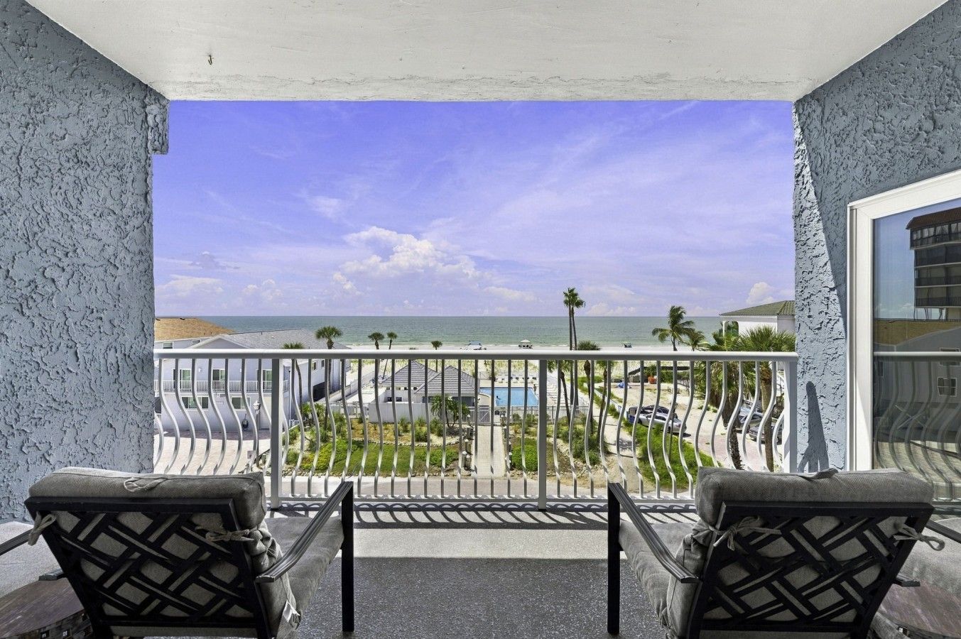 Un balcon avec deux chaises, une piscine et une vue sur la plage.