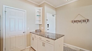 A kitchen with white cabinetry, a granite countertop, and a wall-mounted shelf above the sink.