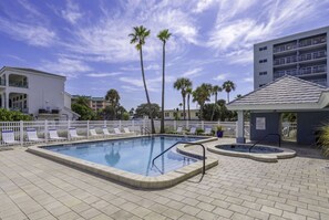 Ein Pool mit Liegestühlen und Palmen, umgeben von Gebäuden.