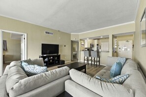 Sala de estar con sofá, una mesa de centro y televisor. Hay una zona de cocina con mesa y sillas.