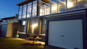 Une maison moderne à deux étages, dotée de grandes fenêtres, d’un patio couvert et d’un garage.