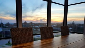 Une pièce dotée d’une grande fenêtre, de trois fauteuils en osier et d’une table en bois.