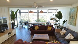 Un salon spacieux doté d’une grande télévision, de sièges confortables et de grandes fenêtres offrant une vue sur l’extérieur.