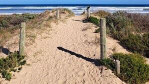 Un sentier de sable bordé de poteaux en bois, qui mène à l’océan.