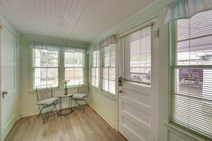 Cozy retreat with a traditional design, featuring a wooden floor and light-colored walls. The room includes a door, window, and a small table with a chair.