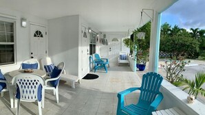 Un espace extérieur abrité, aménagé avec des chaises blanches et bleues, une petite table et des plantes en pot.