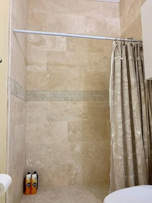 Un espace douche avec des carreaux de couleur beige, un porte-serviettes et un rideau de douche orné d’un motif floral.