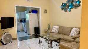 Un salon avec une table basse en verre, un canapé beige et un téléviseur fixé au mur.