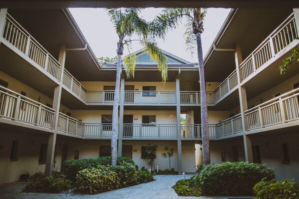 A multi-story building with a central courtyard, balconies, and surrounding greenery.
