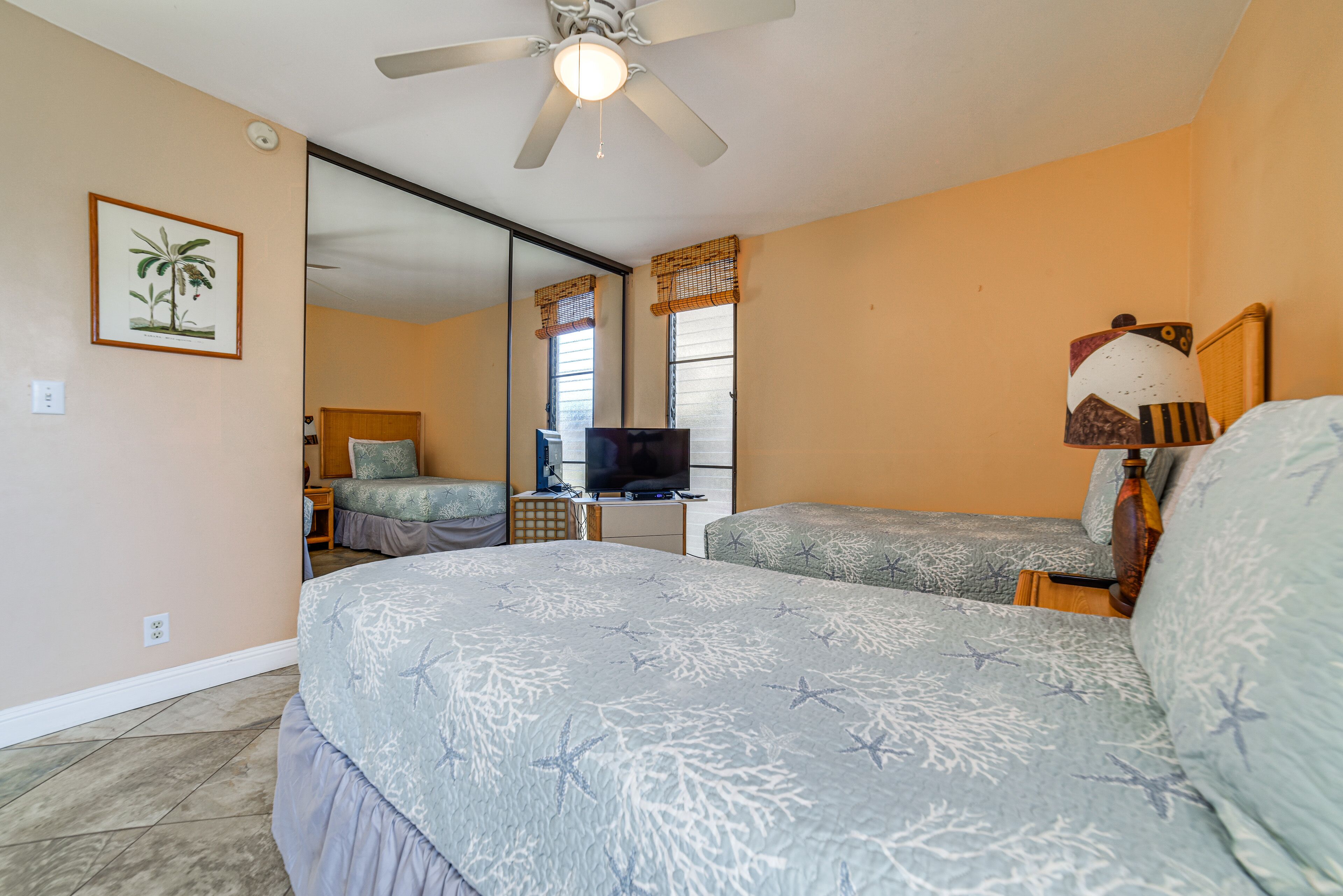 A bedroom with two beds, a ceiling fan, a television, and a large mirror.