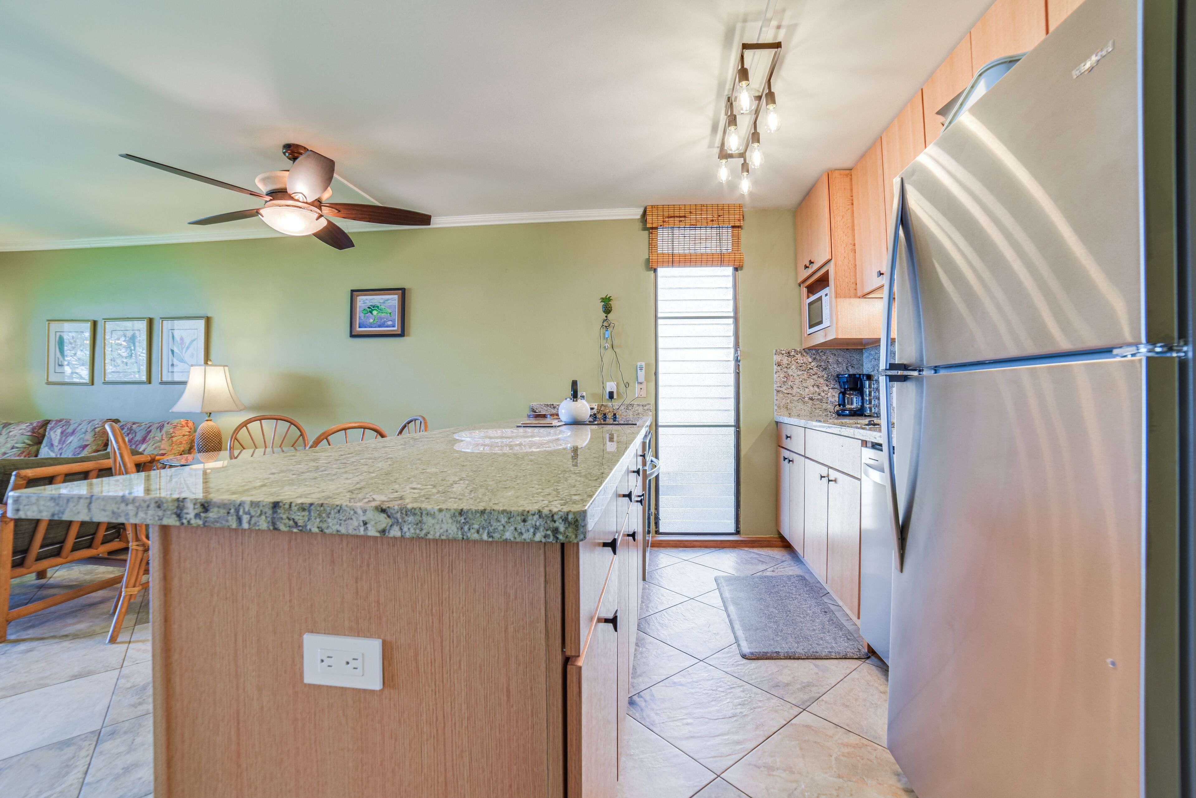 Una cocina con una isla central, armarios de madera, un refrigerador de acero inoxidable y un ventilador de techo.