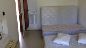 A bedroom with a bed, bedside table, and a door leading to a bathroom. - Casa Praia da Penha (Aracruz)