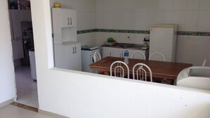 A compact kitchen with white cabinets, a wooden dining table, and a white refrigerator. - Casa Praia da Penha (Aracruz)