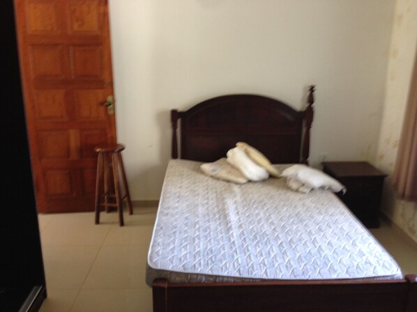 A bedroom with a wooden bed, a nightstand, and a wooden stool.