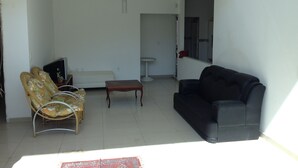 A living room with a sofa, a black armchair, a wooden coffee table, and a wicker chair with cushions. - Casa Praia da Penha (Aracruz)