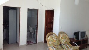 A living room with two wicker chairs, a television on a wooden stand, and a door leading to a bathroom. - Casa Praia da Penha (Aracruz)