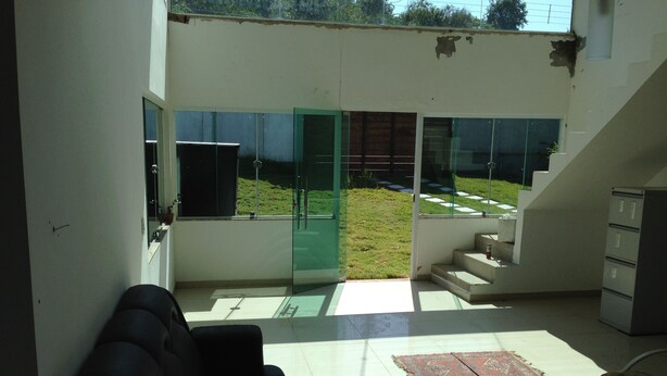 A modern living room with a black sofa, a glass door leading to a balcony, a small rug, and a wicker chair. - Casa Praia da Penha (Aracruz)