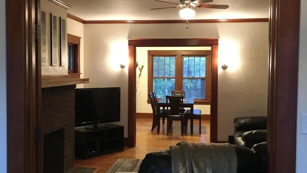 Een woonkamer met een open haard, televisie en een eethoek met tafel en stoelen.
