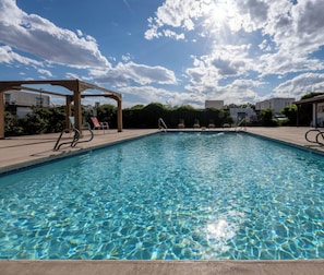 A clear swimming pool with lounge chairs and a pergola structure.