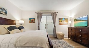 A bedroom with a bed, a TV, a dresser, and a window with curtains.