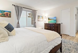 A bedroom with a bed, curtains, a television, a dresser, and a door.