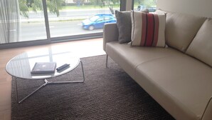 A modern living room with a leather sofa, a glass coffee table, and a view of a street with cars.