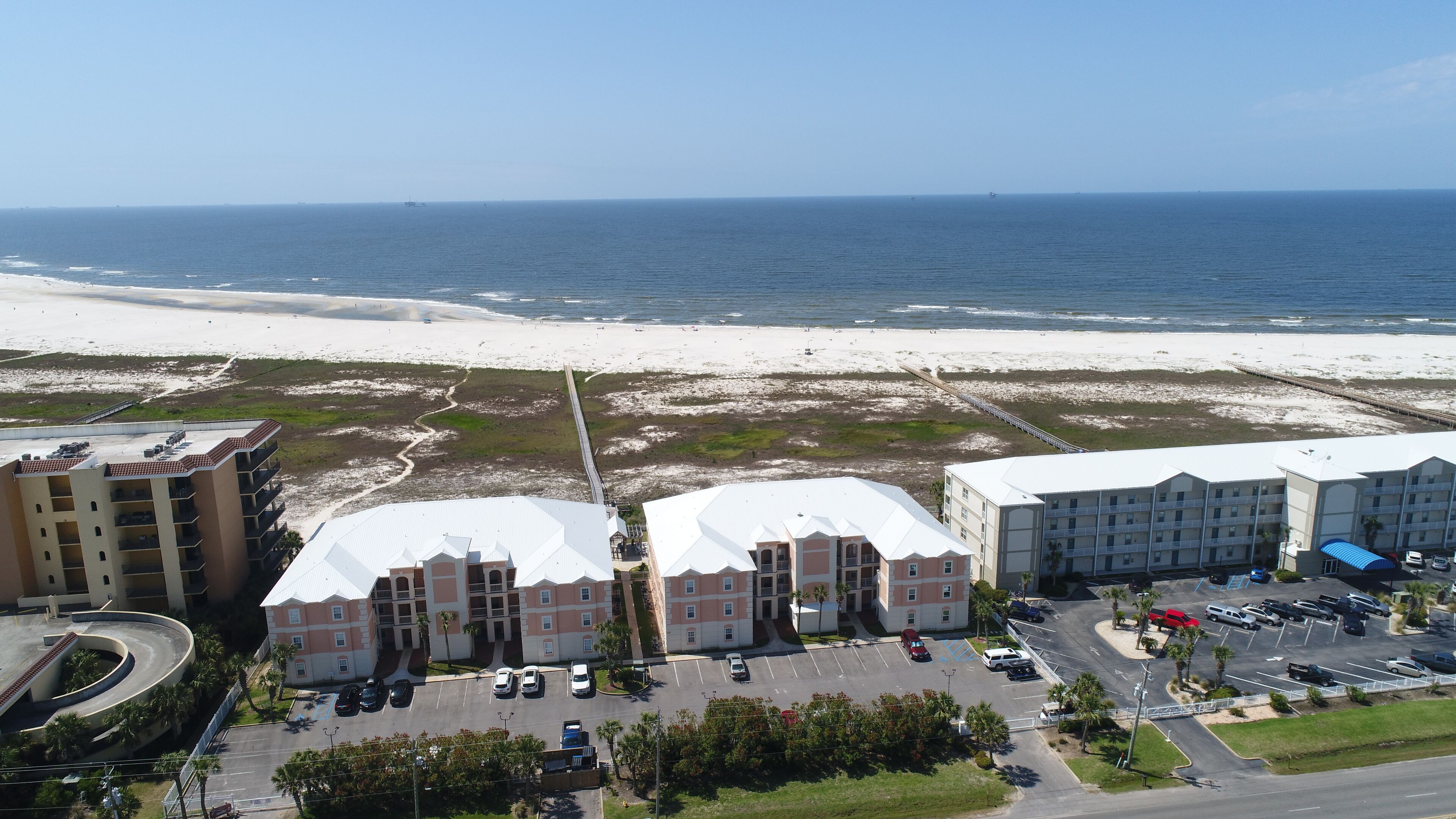 A coastal hotel with multiple buildings, a parking lot, and a beach in the background.