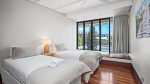 A hotel room with two beds, a nightstand with a lamp, a window with a view of the outside, and a curtain. - Bronze @ Lennox Head (LENNOX HEAD)