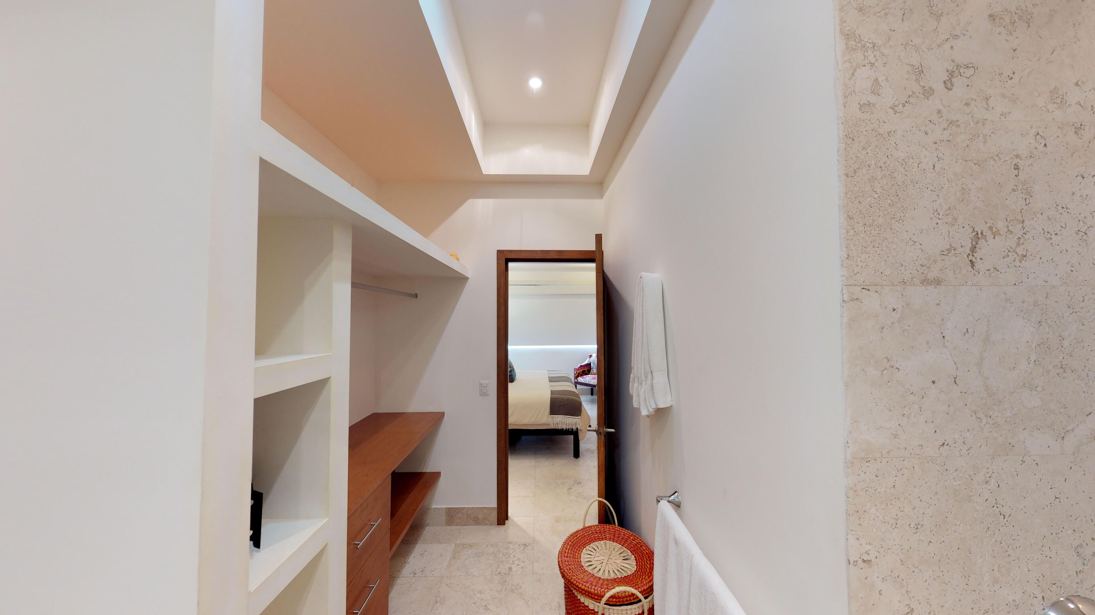 A narrow hallway with a wooden bench, a red woven basket, and a mirror on the wall.