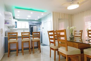 Una cucina moderna con mobili bianchi, forno a incasso e frigorifero. C'è un'area pranzo con un tavolo in vetro e sedie in legno.