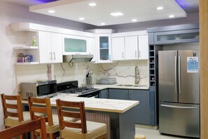 Una cucina moderna con mobili bianchi, frigorifero in acciaio inossidabile, forno a microonde e piano cottura a gas.