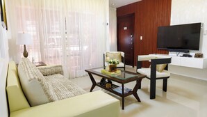 Un salon comprenant un canapé, un fauteuil, une table basse, un téléviseur et une porte.