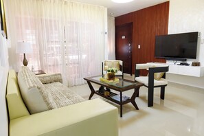 Un salon comprenant un canapé, un fauteuil, une table basse, un téléviseur et une porte.