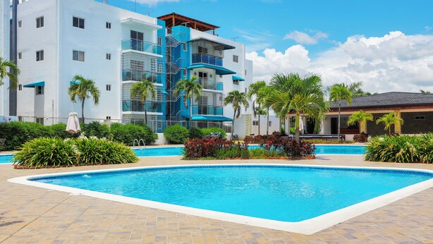 Un hôtel moderne doté d’une piscine, de palmiers et surplombant un ciel d’un bleu limpide.