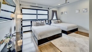 Ein modernes Schlafzimmer mit zwei Betten, einem großen Fenster mit Vorhängen und einem dekorativen Spiegel.